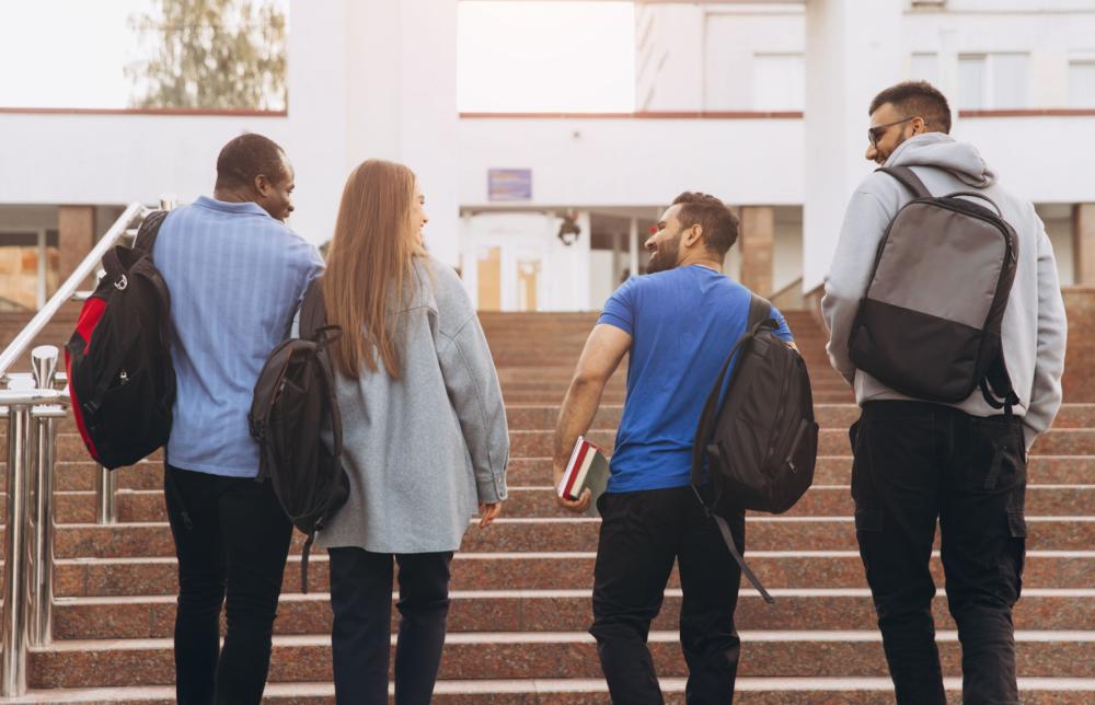 Four college students ascending an outdoor staircase side by side, in a metaphorical exercise of facing the challenges of higher education and life