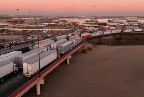 A long line of trucks wait on a bridge crossing at sunset